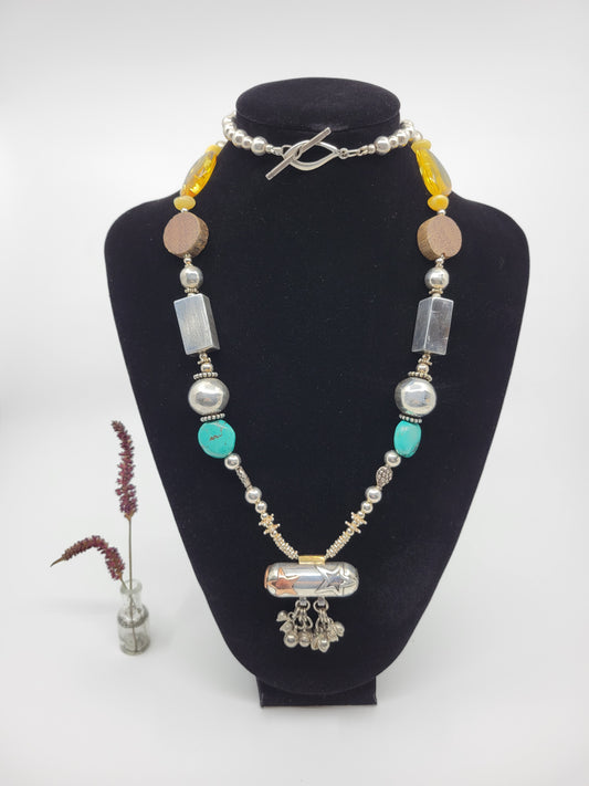 A sterling silver statement piece necklace with baltic amber and turquoise, displayed on a mannequin. The necklace features silver beads, copper and sterling silver stars, and amber beads.